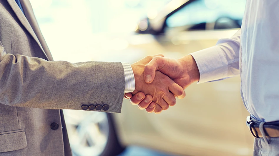 People shaking hands beside a car